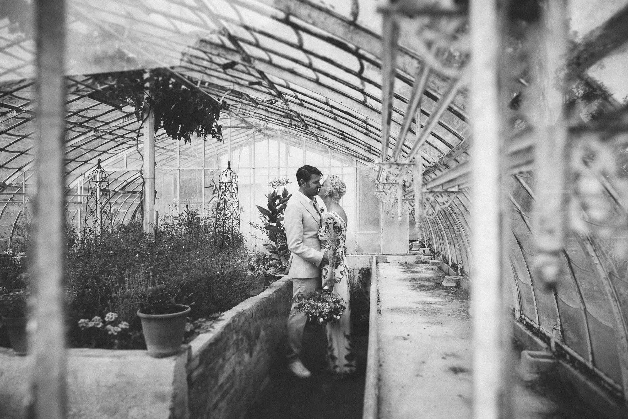 bride and groom kissing green house